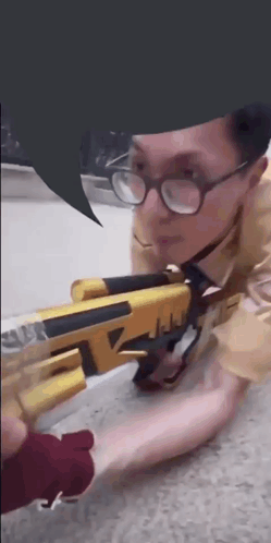 A Man Wearing Glasses Is Kneeling Down With A Gun GIF