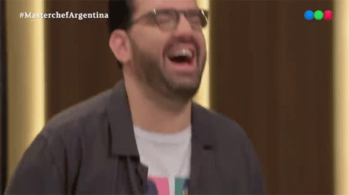 A Man Wearing Glasses Is Laughing In Front Of A Masterchef Argentina Logo GIF