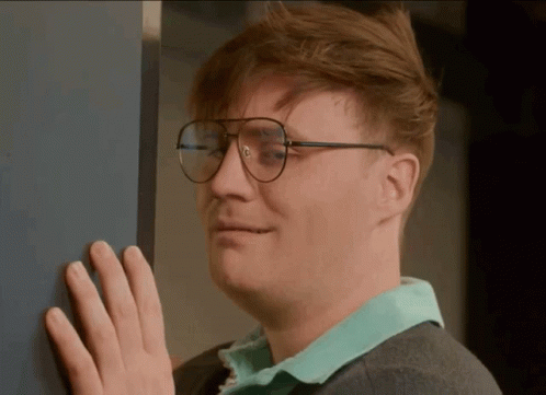 A Man Wearing Glasses Is Leaning Against A Wall With His Hand GIF