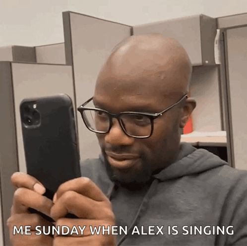 A Man Wearing Glasses Is Looking At His Phone With The Words Me Sunday When Alex Is Singing Below Him GIF