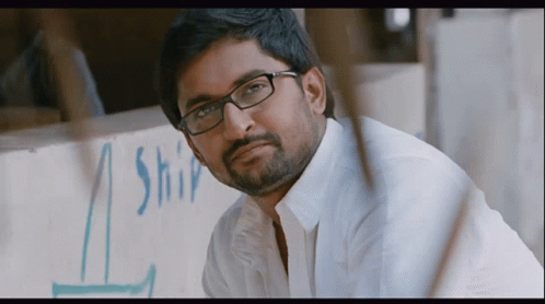 A Man Wearing Glasses Is Looking At The Camera In Front Of A Sign That Says Ship GIF