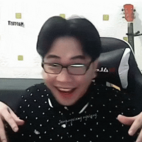 A Man Wearing Glasses Is Making A Funny Face While Sitting In Front Of A Guitar . GIF