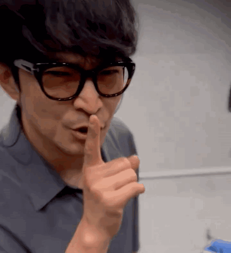 A Man Wearing Glasses Is Making A Shhh Gesture GIF