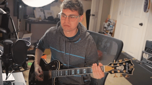 a man wearing glasses is playing a guitar with the brand name gibson on the headstock