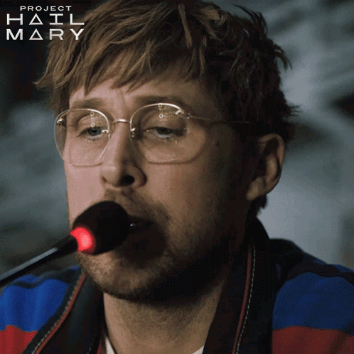 A Man Wearing Glasses Is Singing Into A Microphone With Project Hail Mary Written On The Bottom Right GIF