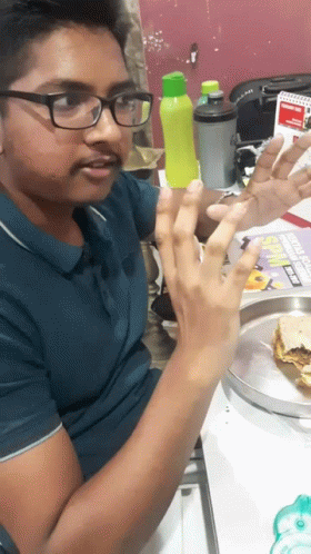 A Man Wearing Glasses Is Sitting At A Table With A Plate Of Food And A Sign That Says Subway GIF