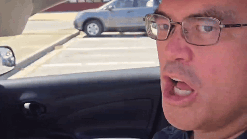 a man wearing glasses is sitting in a car with his mouth open