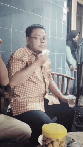 A Man Wearing Glasses Is Sitting In A Chair Eating A Piece Of Food GIF
