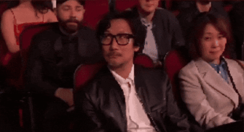 A Man Wearing Glasses Is Sitting In A Theatre Watching A Movie . GIF