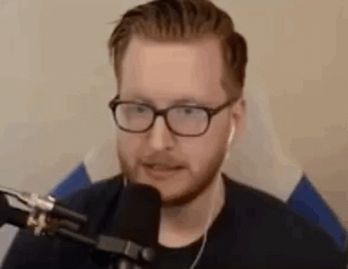 A Man Wearing Glasses Is Sitting In Front Of A Microphone . GIF
