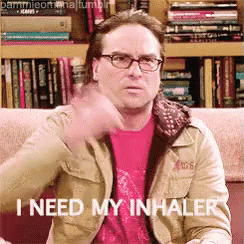 A Man Wearing Glasses Is Sitting On A Couch And Says " I Need My Inhaler " GIF