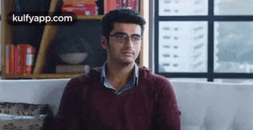 A Man Wearing Glasses Is Sitting On A Couch In A Living Room . GIF