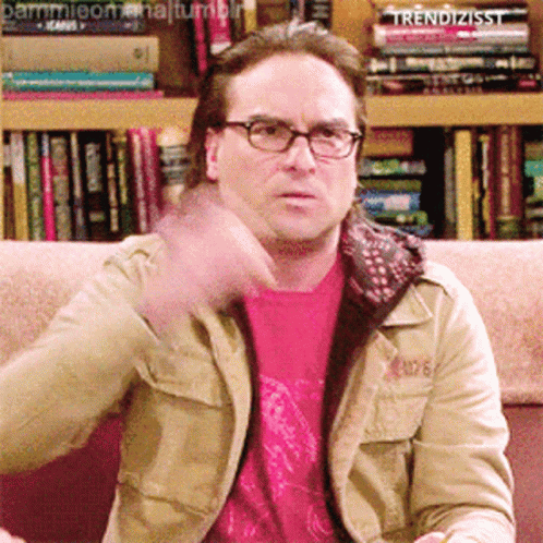 A Man Wearing Glasses Is Sitting On A Couch In Front Of A Bookshelf That Says Trendizisst On It GIF