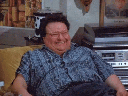 A Man Wearing Glasses Is Sitting On A Couch Laughing . GIF