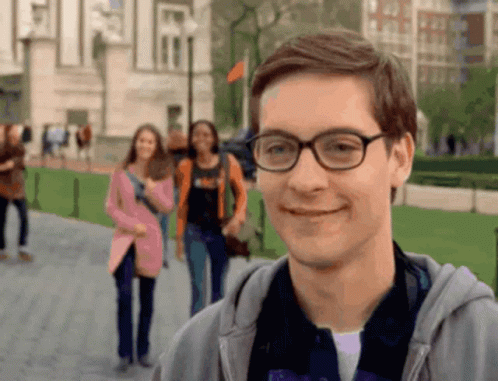 A Man Wearing Glasses Is Smiling In Front Of A Blurry Group Of People GIF