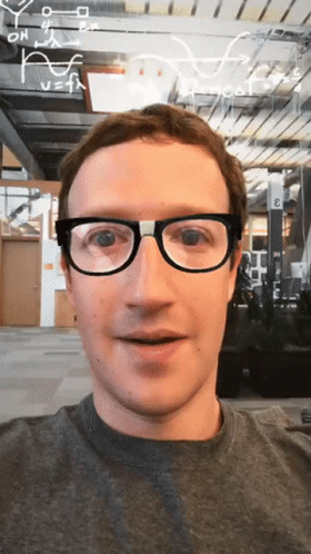 A Man Wearing Glasses Is Smiling In Front Of A Sign That Says " E " On It GIF