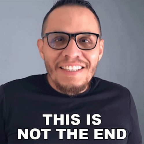 A Man Wearing Glasses Is Smiling In Front Of A Sign That Says " This Is Not The End " GIF