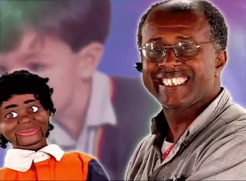 a man wearing glasses is smiling while holding a puppet .