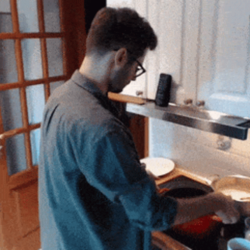 A Man Wearing Glasses Is Standing In A Kitchen Cooking GIF