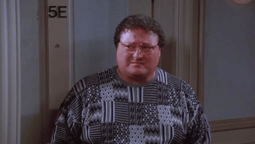 A Man Wearing Glasses Is Standing In Front Of A Door That Says 5E . GIF