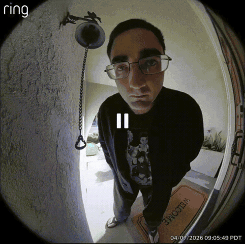 A Man Wearing Glasses Is Standing In Front Of A Door With A Welcome Mat GIF