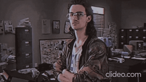 A Man Wearing Glasses Is Standing In Front Of A Sign That Says " Heckerman " GIF