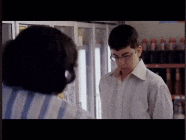A Man Wearing Glasses Is Standing Next To A Woman In A Striped Shirt GIF