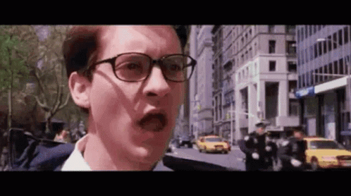 A Man Wearing Glasses Is Standing On A City Street With A Shocked Look On His Face . GIF