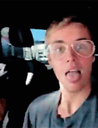 A Man Wearing Glasses Is Sticking His Tongue Out In A Car GIF
