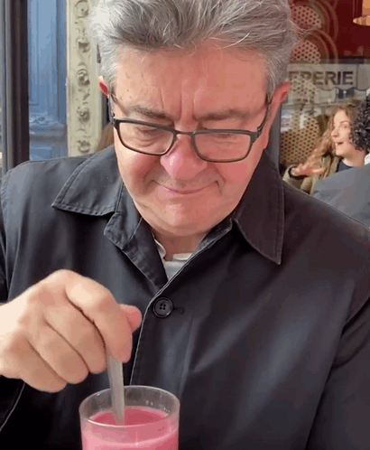 A Man Wearing Glasses Is Stirring A Pink Drink GIF