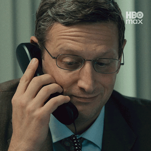 A Man Wearing Glasses Is Talking On A Telephone With Hbo Max Written On The Bottom GIF