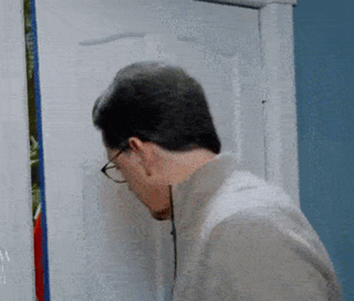 A Man Wearing Glasses Looks Through A Hole In A Door GIF