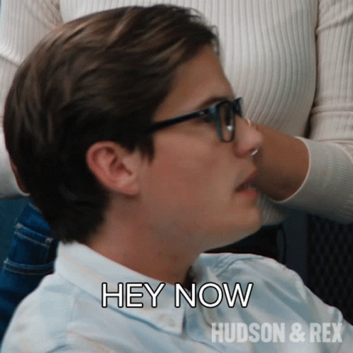 A Man Wearing Glasses Says " Hey Now " In Front Of A Woman GIF