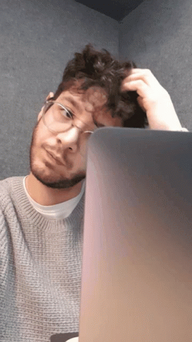 A Man Wearing Glasses Scratches His Head While Looking At A Laptop Screen GIF