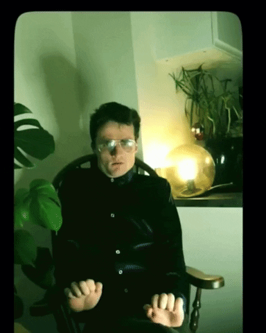 A Man Wearing Glasses Sits In A Chair GIF