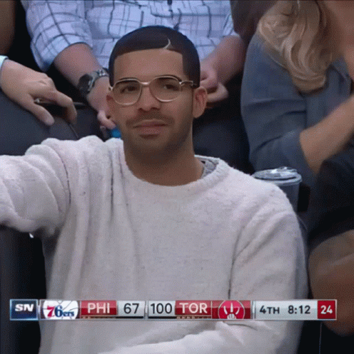 A Man Wearing Glasses Sits In A Stadium Watching A Basketball Game Between The 76Ers And The Tor GIF