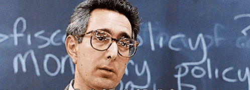 A Man Wearing Glasses Stands In Front Of A Blackboard That Says " Fiscal Theory " GIF