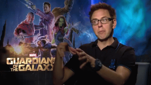A Man Wearing Glasses Stands In Front Of A Poster For Guardians Of The Galaxy GIF