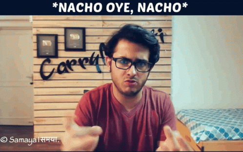 A Man Wearing Glasses Stands In Front Of A Wall That Says Nacho Oye Nacho GIF