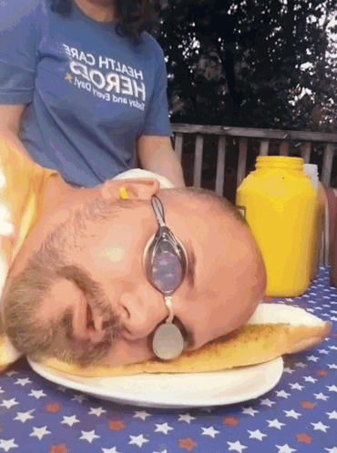 A Man Wearing Goggles Is Laying On A Plate With His Head On A Slice Of Pizza GIF