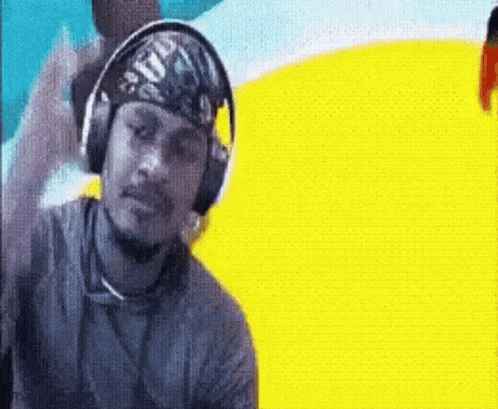 A Man Wearing Headphones And A Bandana On His Head Is Standing In Front Of A Yellow Background . GIF