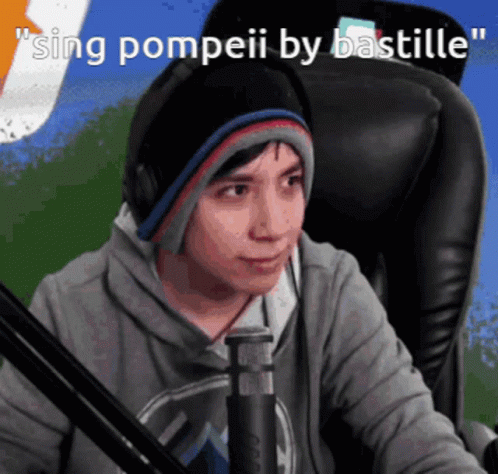 A Man Wearing Headphones And A Beanie Is Singing Pompeii By Bastille In Front Of A Microphone GIF