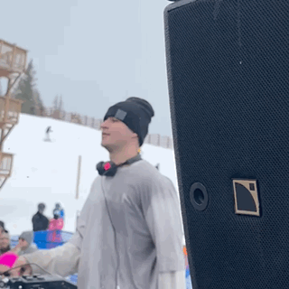 A Man Wearing Headphones And A Beanie Is Standing In Front Of A Speaker GIF