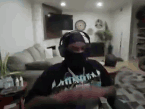 A Man Wearing Headphones And A Black Mask Is Dancing In A Living Room . GIF