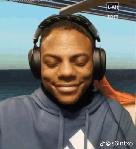 a man wearing headphones and a blue adidas sweatshirt smiles