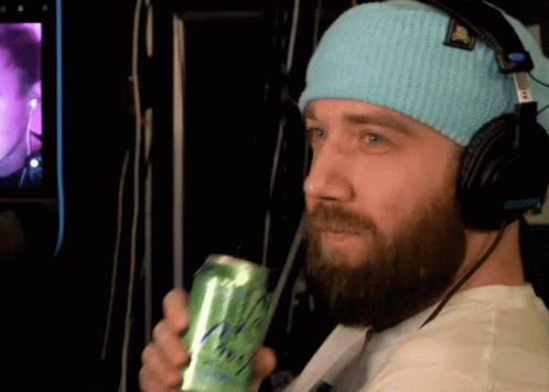 A Man Wearing Headphones And A Blue Beanie Holds A Green Can GIF