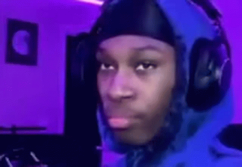 A Man Wearing Headphones And A Blue Hoodie Is Making A Funny Face In A Room With Purple Lights . GIF