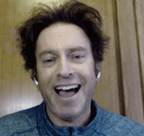 A Man Wearing Headphones And A Blue Shirt Is Smiling GIF
