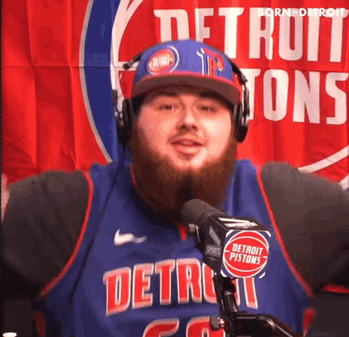 A Man Wearing Headphones And A Detroit Pistons Jersey Stands In Front Of A Microphone GIF