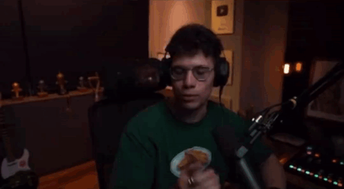 A Man Wearing Headphones And A Green Shirt Is Standing In Front Of A Microphone And Giving The Middle Finger . GIF